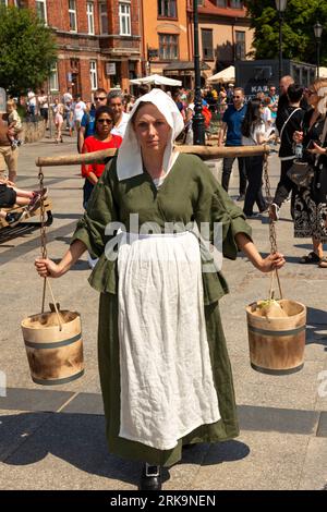 Weibliche Reendarstellerin, die als mittelalterliche Straßenverkäuferin auf dem Targ Rybny oder Fischmarkt in der Altstadt von Danzig, Polen, gekleidet ist Stockfoto