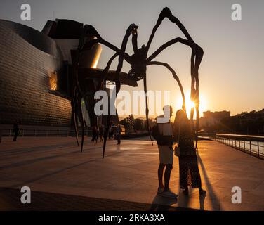 Bilbao, Spanien - 02. August 2022: Ein paar Touristen machen ein Selfie bei Sonnenuntergang neben der Spinne, der Skulptur von Louise Bourgeois mit dem Titel Mamam in Th Stockfoto