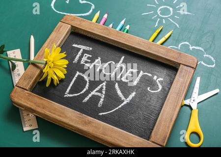 Blackboard with text TEACHER'S DAY, beautiful flower and stationery on green background Stock Photo