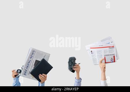 Female hands with newspapers, notebook, microphone and photo camera on light background Stock Photo