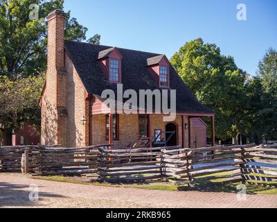 On a sunny day with a blue sky in Williamsburg, Virginia, USA, stands a historic red brick building complemented by a wooden fence. Stock Photo