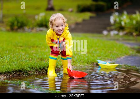 Kind spielt mit Papierboot in der Pfütze. Bei Herbstregen spielen Kinder im Freien. Herbstregenwetter Outdoor-Aktivität für kleine Kinder. Stockfoto