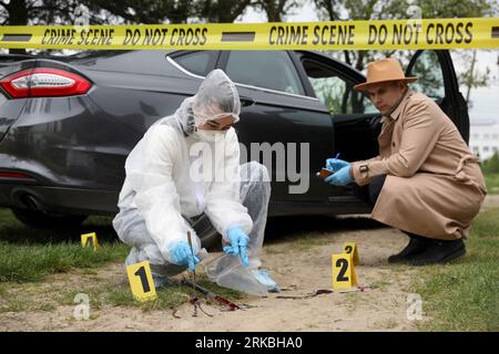 Investigator and criminologist working with evidences at crime scene near car outdoors Stock Photo