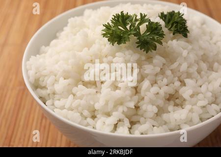 Bowl with delicious rice and parsley on bamboo mat, closeup Stock Photo