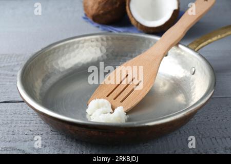 Bratpfanne mit Bio-Kokosöl und Spatel auf grauem Holztisch, Nahaufnahme Stockfoto