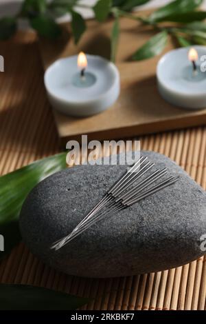 Stein mit Akupunkturnadeln auf Bambusmatte Stockfoto