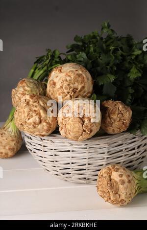 Fresh raw celery roots in wicker basket on white wooden table Stock Photo