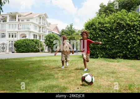 Geschwister, die nach der Schule im Hinterhof Fußball spielen Stockfoto