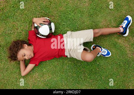Müder Junge, der nach dem Fußballspielen auf dem Rasen ruht, Blick von oben Stockfoto