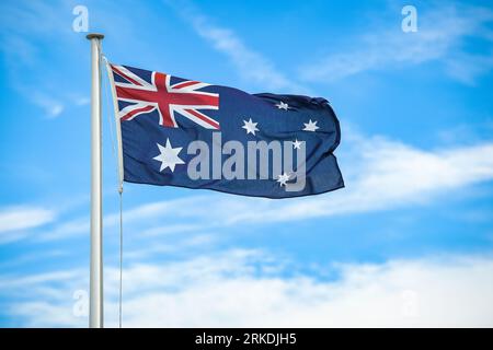 Australian flag flying on a flagpole with clouds and blue sky in the background Stock Photo