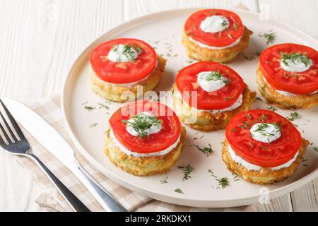 Homemade fried zucchini in egg batter served with creamy garlic sauce, dill and fresh tomatoes close-up in a plate on the table. Horizontal Stock Photo