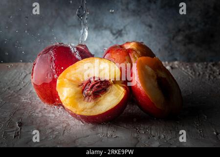 Wasserspritzer auf drei Nektarinen. Rustikaler Tisch mit Obst. Die Früchte des Sommers. Gebrochener Pfirsich. Stockfoto