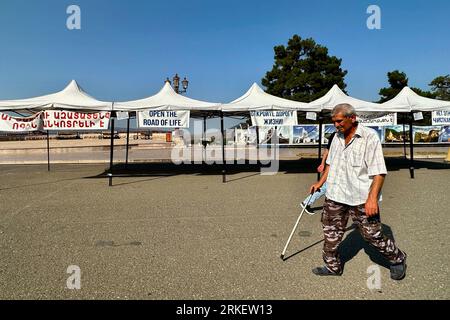 PRODUKTION - 23. August 2023, Aserbaidschan, Stepanakert: Ein Mann geht über einen leeren Platz, vorbei an einem Pavillon, auf dem ein Poster mit der Aufschrift "Öffnen Sie die Straße des Lebens" hängt. In der Region Berg-Karabach im Kaukasus, tief im Süden der ehemaligen Sowjetunion, kommt die Situation bedrohlich. Seit Dezember 2022 hat Aserbaidschan, zu dem das Gebiet völkerrechtlich gehört, die Lebensader der Karabach-Armenier zum nahegelegenen Mutterland Armenien blockiert. Armenier in der international nicht anerkannten Entität fürchten Hunger. Schätzungen liegen zwischen 100.000 und 120.000 Personen. Seit Dem 20. Dezember Stockfoto