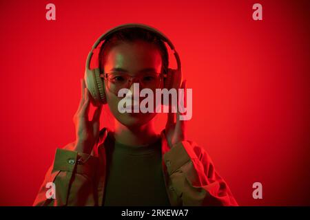Porträt einer jungen asiatischen Frau mit Brille und Kopfhörer und Blick auf die Kamera Stockfoto