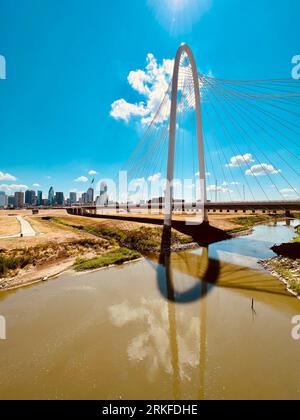 The Margaret Hunt Hill Bridege in Dallas Texas spans a river on a bright, sunny day with stunning city skylines in the background Stock Photo