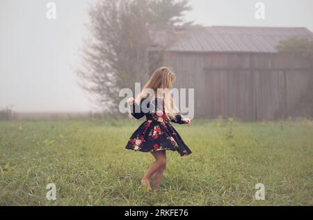 Das junge Mädchen wirbelt allein an einem nebeligen Morgen auf einem verlassenen Bauernhof Stockfoto
