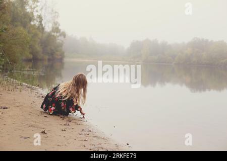 Ein nebliger Blick auf den See am Morgen mit einem kleinen Mädchen mit wilden Haaren Stockfoto