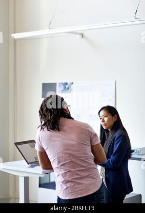 Rückansicht eines Geschäftsmannes, der mit einer Geschäftsfrau am Schreibtisch gegen die Wand im Büro diskutiert Stockfoto