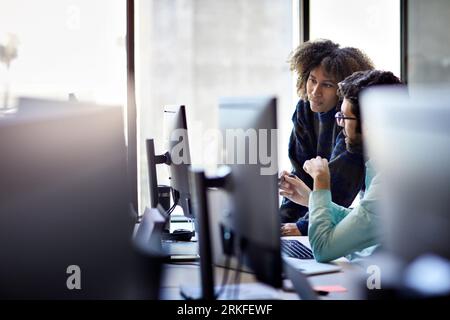 Confident colleagues discussing over desktop computer against window in office Stock Photo