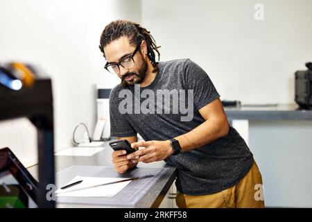 Confident businessman using smart phone while standing by table in office Stockfoto