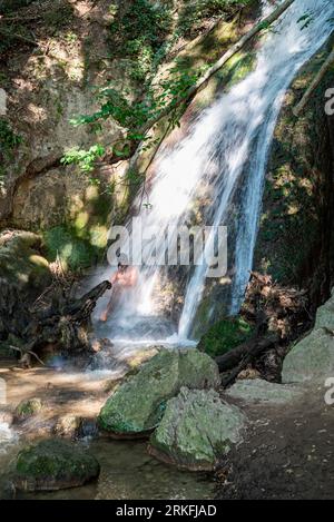 Mensch unter einem Wasserfall im Wald. Stockfoto