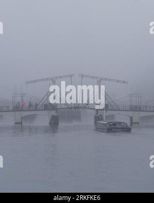 Amsterdam, Niederlande - November 27 2022: Die weltberühmte dünne Brücke in Amsterdam, die an einem Herbstmorgen im November von Nebel umgeben ist. Stockfoto