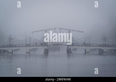 Amsterdam, Niederlande - November 27 2022: Die weltberühmte dünne Brücke in Amsterdam, die an einem Herbstmorgen im November von Nebel umgeben ist. Stockfoto