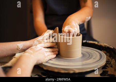 Hände eines jungen Mädchens und eines Kindes, die eine Tasse auf Potter's Whe kreieren Stockfoto