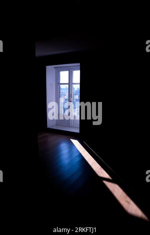 Ein heller Sonnenstrahl filtert durch ein großes Fenster in einem geräumigen, leerstehenden Raum Stockfoto