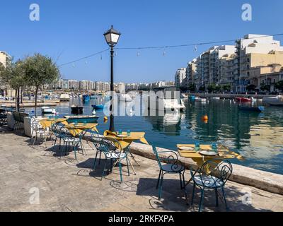 San Giljan (St. Julian's) Malta - 7. August 2022: Tisch und Stühle an der Promenade entlang der Spinola Bay. Stockfoto