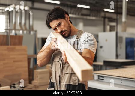 Junger Zimmermann sucht und wählt Holzbohle in einer Werkstatt in einer Holzfabrik Stockfoto