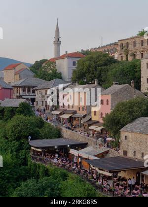 Altstadt in Mostar, Bosnien und Herzegowina, mit Cafés, Restaurants, Steinmauern und farbenfrohen Häusern und Minarett darüber. August 2023. Stockfoto