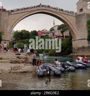 Die Menschen beobachten, wie ein Brückenspringer von Stari Most (Alte Brücke) am 23. August 2023 in Mostar, Bosnien und Herzegowina, auf das Wasser trifft. Stockfoto