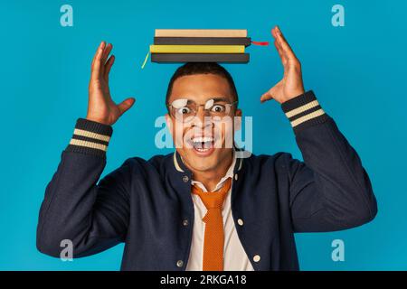 Staunende afroamerikanische Studenten posierten mit Notizbüchern auf dem Kopf auf blauem Hintergrund, Brille und stylischer Jacke Stockfoto