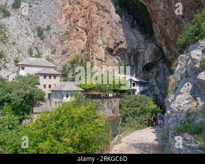 Das Blagaj-Kloster (oder Blagaj Tekija) am Fluss Buna mit Touristen auf einem Pfad im Vordergrund in der Nähe von Mostar, Bosnien und Herzegowina, 24. August 2023. Stockfoto