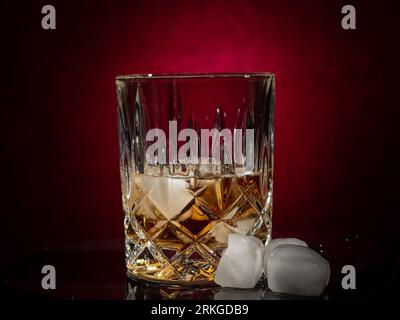 Ein isoliertes Bild eines mit einem klaren alkoholischen Getränk gefüllten Highballglases, das auf einem Eisblock ruht und über den Eisbrocken verteilt sind Stockfoto