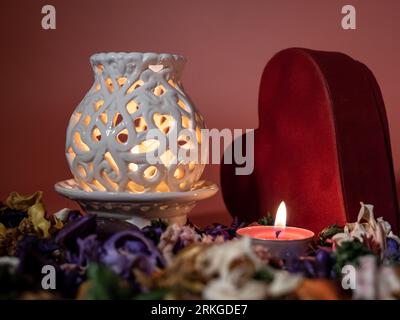 A lit candle in a glass holder is placed in the center of a heart-shaped box with a lid, surrounded by a heart-shaped pattern Stock Photo