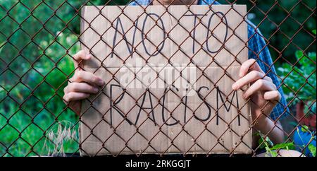 Junger Mann, der ein Poster hinter Gittern hält, nein zum Rassismus Stockfoto