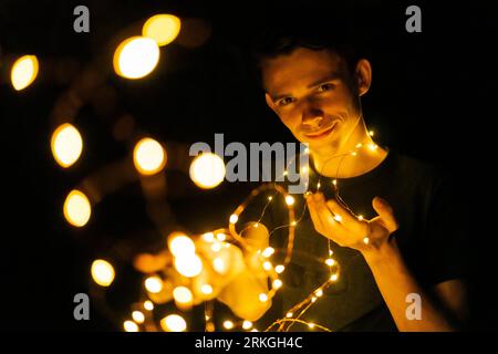 Junger Mann in der Nacht, der glühende Girlanden in den Händen hält, selektiver Fokus Stockfoto