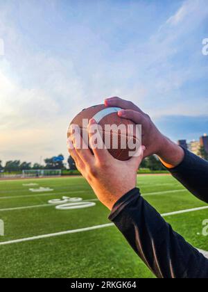 The hands catching an American football ball in a green field Stockfoto