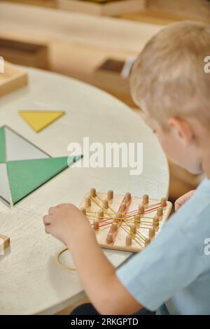 boy playing with rubber bands and wooden sticks during lesson in montessori school Stock Photo