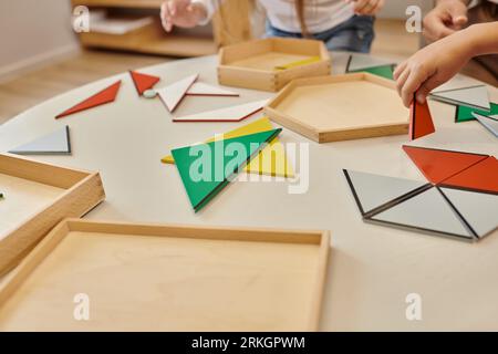 Abgeschnittene Ansicht von Lehrern und Kindern, die mit Dreiecken auf dem Tisch in der montessori-Schule spielen Stockfoto