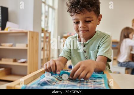 smiling african american boy playing with cloth and buttons in montessori school Stock Photo