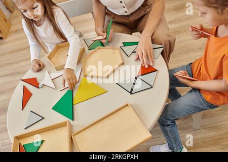 Blick auf Lehrer und Kinder, die mit Dreiecken auf dem Tisch in der montessori-Schule spielen Stockfoto