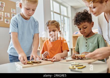 Interrassische Kinder spielen mit didaktischem montessori-Material in der Nähe des Lehrers in der Schule, lernen und spielen Stockfoto