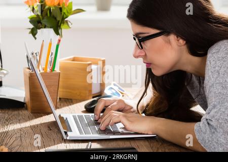 Geschäftsfrau, Sitzen in der falschen Haltung Arbeiten am Laptop auf Holz- Büro Schreibtisch Stockfoto