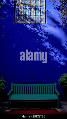A wooden bench in front of a blue building with a window. Stockfoto