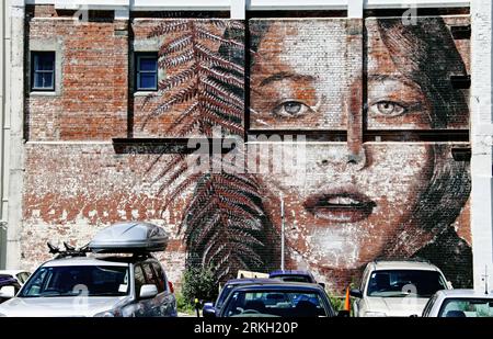 A row of cars parked in front of a mural of a female on a brick wall in Christchurch, New Zealand Stock Photo