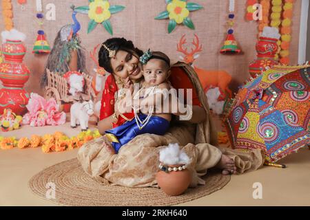 Janmashtami-Konzept. Mutter sitzt mit ihrem süßen Jungen, der als kleine krishna verkleidet ist. Stockfoto