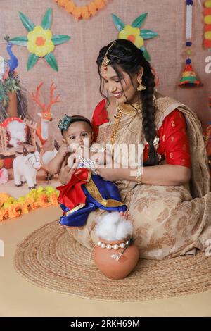 Janmashtami-Konzept. Mutter sitzt mit ihrem süßen Jungen, der als kleine krishna verkleidet ist. Stockfoto